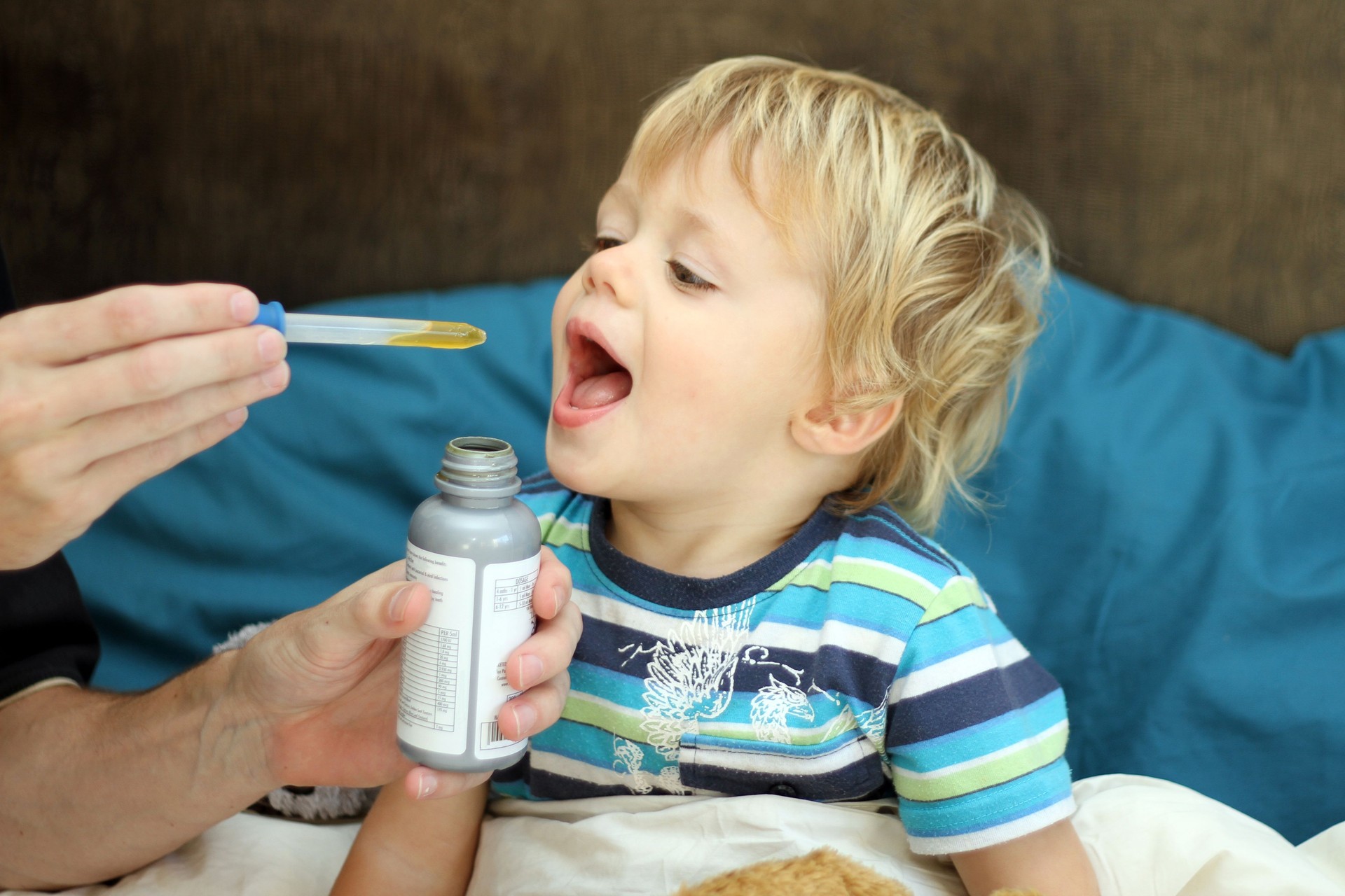 Hands administrating medicine to young boy 