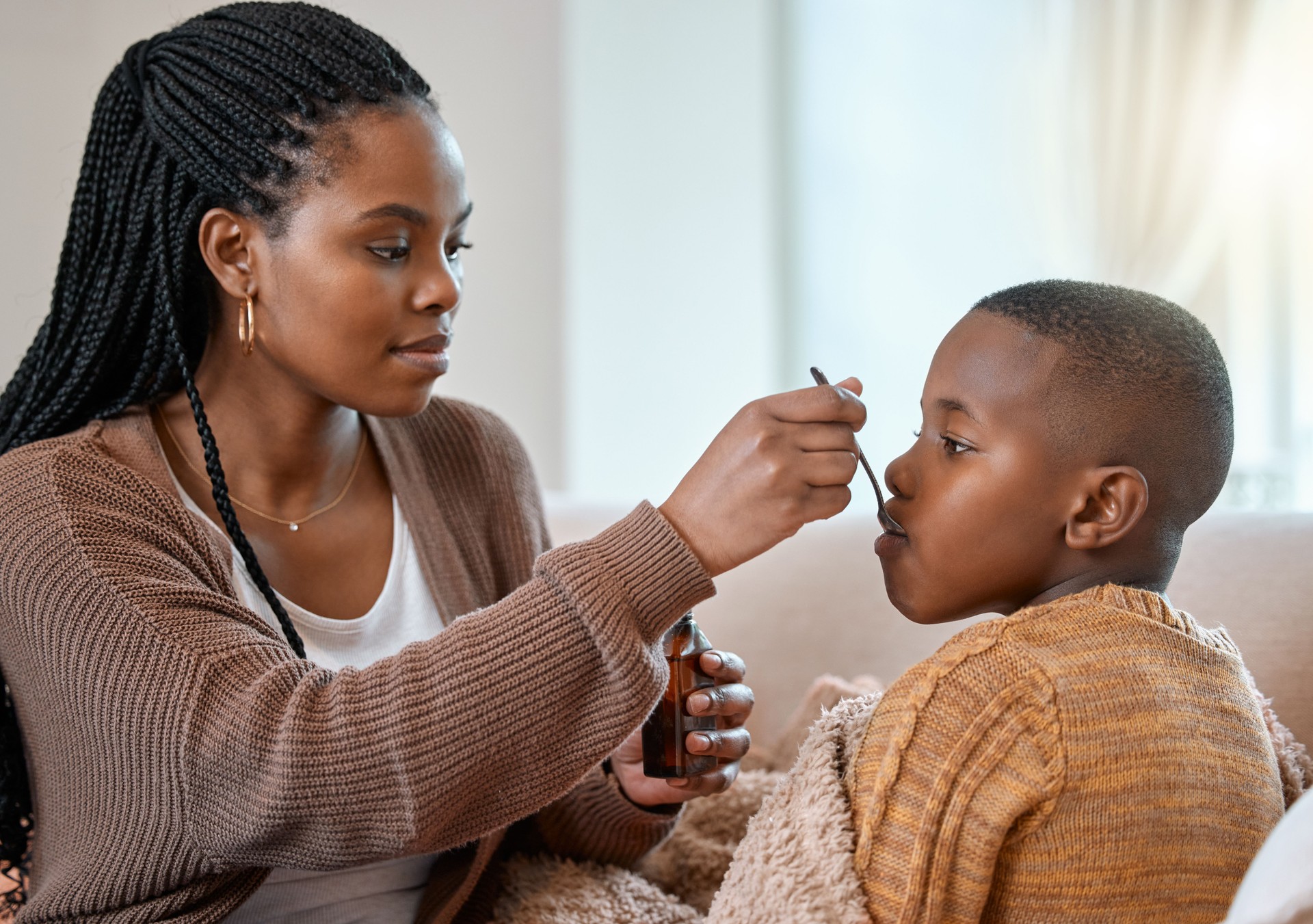 Shot of a young mother giving her sick son cough syrup at home